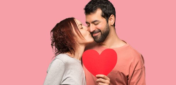 Couple in valentine day holding a heart symbol and kissing over isolated pink background - Photo, Image