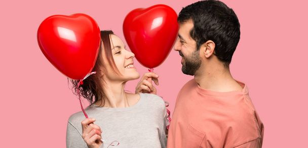 Pár v valentine den drží symbol srdce a balóny nad izolované růžové pozadí - Fotografie, Obrázek