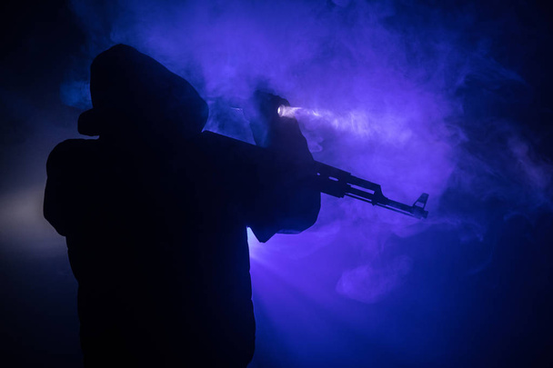 Silhouette di uomo con fucile d'assalto pronto ad attaccare su sfondo scuro tonica nebbia o pericoloso bandito tenendo la pistola in mano. Tiro terrorista con decorazione a tema arma
 - Foto, immagini