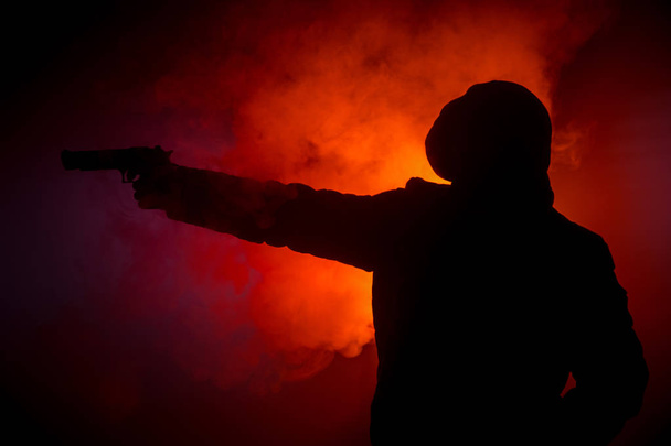 Silhouette des Mannes mit Pistole bereit zum Angriff auf dunkel getönten nebligen Hintergrund oder gefährlichen Banditen mit Waffe in der Hand. Erschießung eines Terroristen mit Waffenmotiv - Foto, Bild