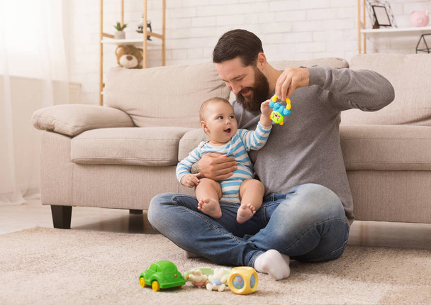 Счастливый отец играет со своим маленьким сыном с яркой погремушкой
 - Фото, изображение