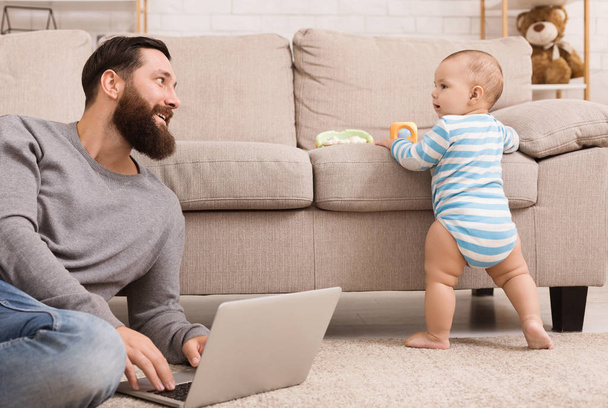 Jeune papa travaillant sur un ordinateur portable et prenant soin de son fils bébé
 - Photo, image