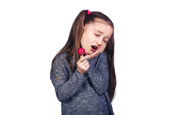 little sad girl with a red lollipop in her hands, whose teeth hurt. - Foto, Bild