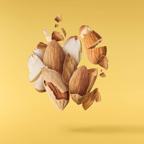 Flying in air fresh raw whole and cut almonds  isolated on yellow background. Concept of Almonds is torn to pieces close-up. High resolution image - Photo, Image