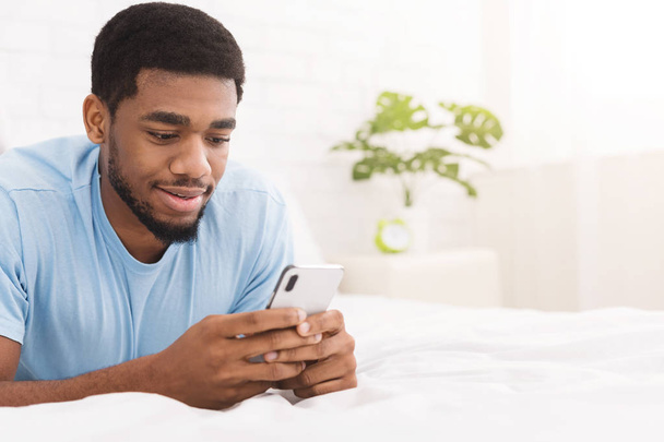 Relaxed casual man using smart phone lying on bed - 写真・画像