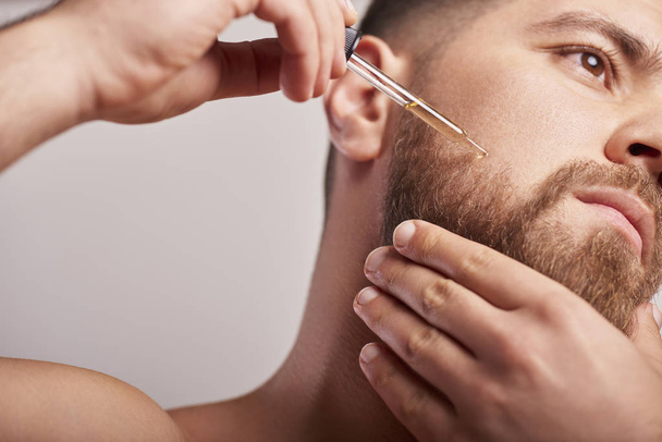 Imagem de close-up de homem bonito segurando pipeta com óleo para barba
 - Foto, Imagem
