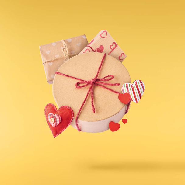 Valentines day concept.  Creative valentines day conception made by falling in air gift boxes and red hearts isolated on yellow background - Photo, Image