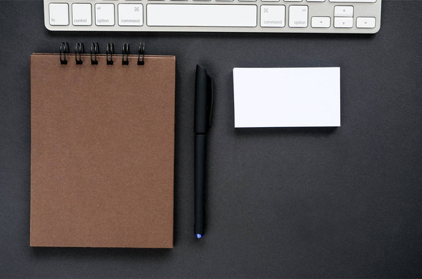 A sketchpad with brown pages, a keyboard and empty business cards on a black background - Photo, Image