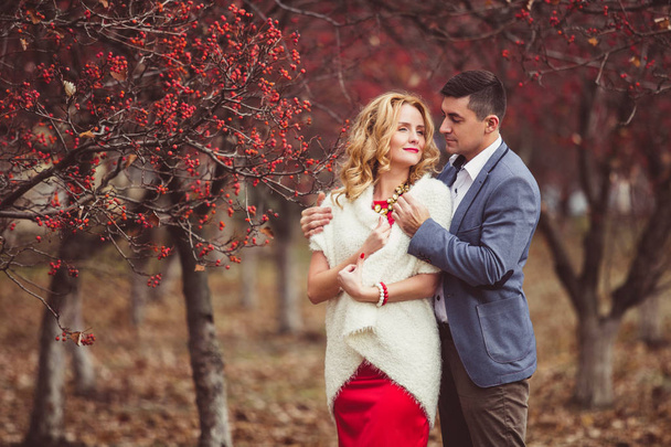 Elegant man embracing shoulders of a beautiful woman on a background of red berries - Фото, зображення
