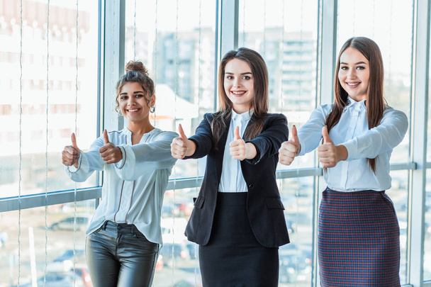 Three young business girls in the office. Dressed in classic clothing style, showing thumbs up - Фото, зображення