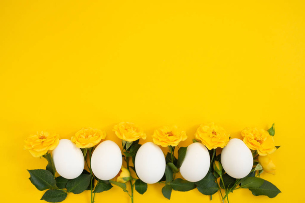 Frame made of flowers and eggs on a yellow background - 写真・画像