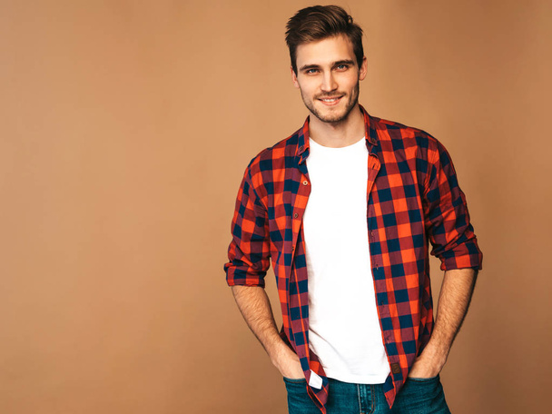 Portrait of handsome smiling stylish hipster lumbersexual businessman model dressed in red checkered shirt. Fashion man posing on golden background - Valokuva, kuva