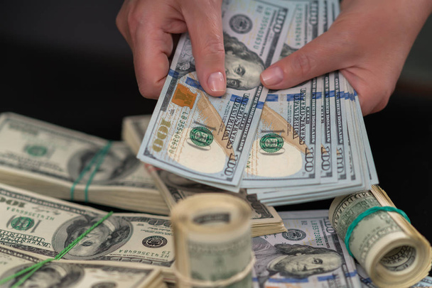 Kobieta trzyma garść podsycana 100 banknotów Usd przez stosy pieniędzy na stole w płatności, biznes, sukces lub uszkodzeniem koncepcja w blisko się na jej ręce - Zdjęcie, obraz