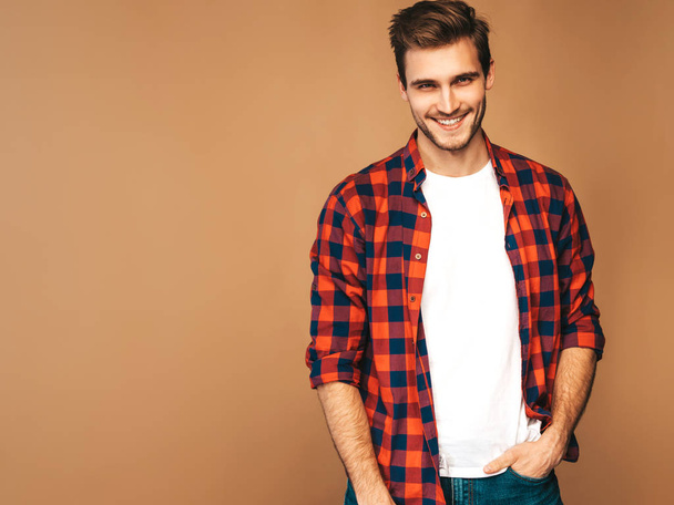 Portrait of handsome smiling stylish hipster lumbersexual businessman model dressed in red checkered shirt. Fashion man posing on golden background - Φωτογραφία, εικόνα