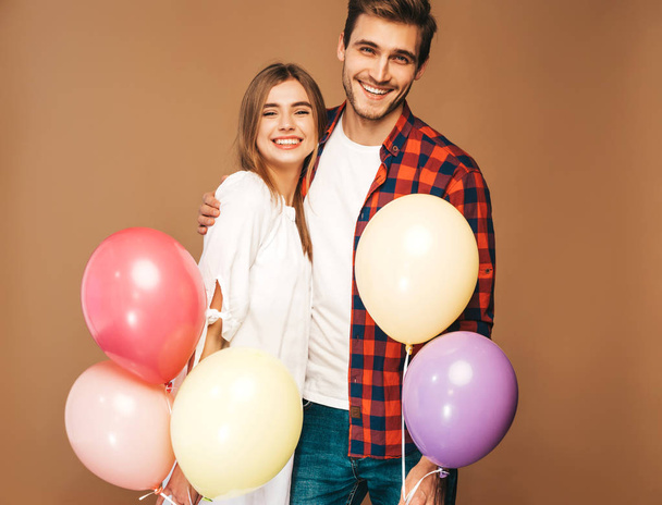 Portrait of Smiling Beautiful Girl and her Handsome Boyfriend holding bunch of colorful air balloons and laughing. Happy Family. Love. Happy Valentine's Day. Posing on golden wall - Zdjęcie, obraz