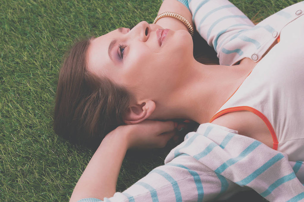 Beautiful young woman lying on green grass - 写真・画像