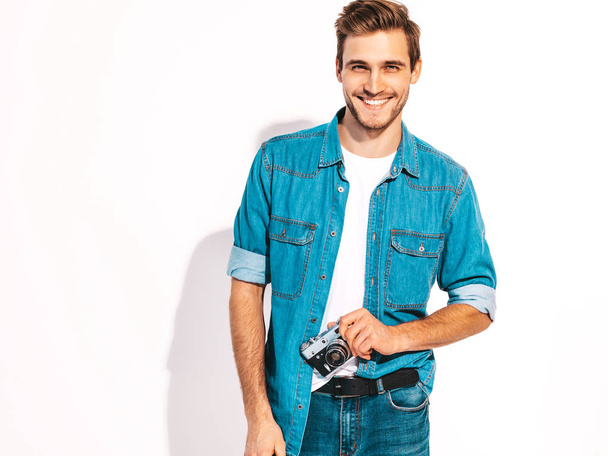 Portrait of handsome smiling man wearing summer hipster jeans clothes. Model male taking picture on old vintage photo camera. Isolated on white - Fotó, kép