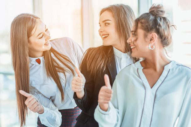 Three young business girls in the office. Dressed in classic clothing style, showing thumbs up with a gesture with copy space - Foto, afbeelding