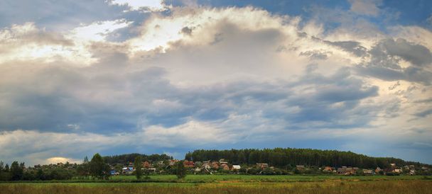 Γραφικό αγροτικό τοπίο. Γραφική ουρανός με τα σύννεφα, σπίτια και δέντρα. Πανοραμικό στιγμιότυπο. - Φωτογραφία, εικόνα
