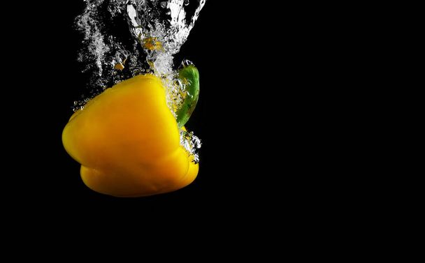 Yellow paprika falling in water with splash on black background. Space for text. - 写真・画像