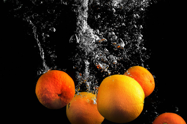Clementine che cadono in acqua con spruzzi su fondo nero
. - Foto, immagini