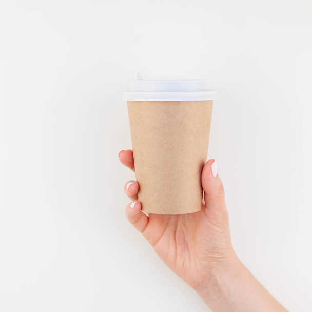 Imagen de maqueta cuadrada de la mano de mujer sosteniendo taza de café de papel artesanal con espacio de copia aislado sobre fondo blanco en estilo minimalista. Plantilla para blog femenino, redes sociales
 - Foto, Imagen