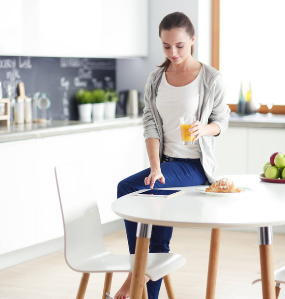 Young woman with orange juice and tablet in kitchen. - Photo, image