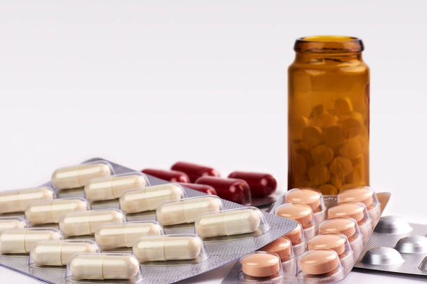 Visão de close-up de pílulas coloridas e cápsulas de frascos de medicamentos castanhos em fundo branco desfocado com espaço para texto
 - Foto, Imagem