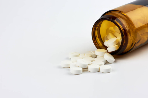 Visão de perto de pílulas e medicamentos polvilhados de um frasco marrom em medicina em um fundo branco
 - Foto, Imagem