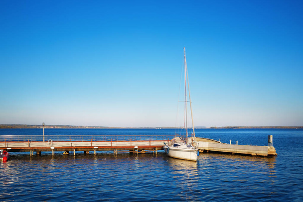 Jacht op de pier. Blauwe wolkenloze lucht en reflectie in het water. Ruimte voor tekst. - Foto, afbeelding