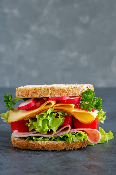 Graham Brotsandwich mit Schinken, Käse und frischem Gemüse auf dunklem Hintergrund. Frühstückskonzept. Gesundes Sandwich mit Schinken, Käse und frischem Gemüse auf einem dunklen Brett. Frühstückskonzept. - Foto, Bild