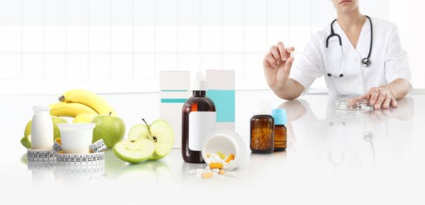 nutritionist doctor shows the pill in his hand at the desk office with apple, fruits, yogurt, tape meter and supplements drugs, healthy and balanced diet concept, web banner and copy space template - Photo, Image