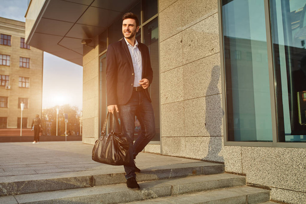 Men's fashion. A young male businessman in a trendy suit and a white shirt with a big black handbag comes out from a fashionable clothing store. - Foto, imagen