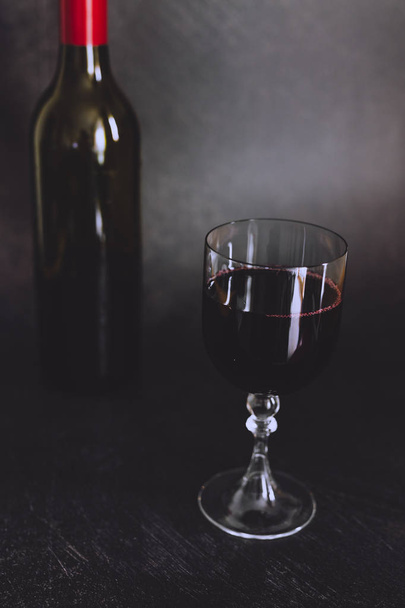 glass of intensely coloured red wine and bottle on dark background, concept of elegant or expensive wine choices - Photo, Image