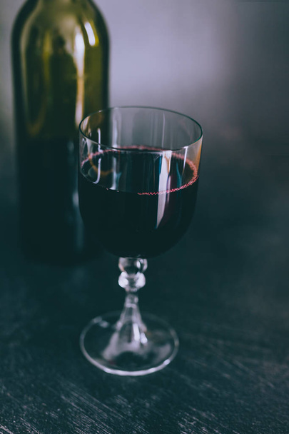 glass of intensely coloured red wine and bottle on dark background, concept of elegant or expensive wine choices - Photo, image
