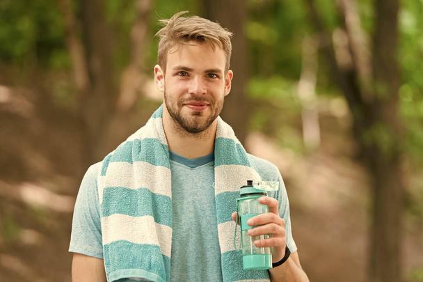 Drink some water. Man jogger with towel on shoulders holds water bottle. Man athlete sport clothes refreshing. Sport and healthy lifestyle concept. Athlete drink water after training in park - Fotografie, Obrázek