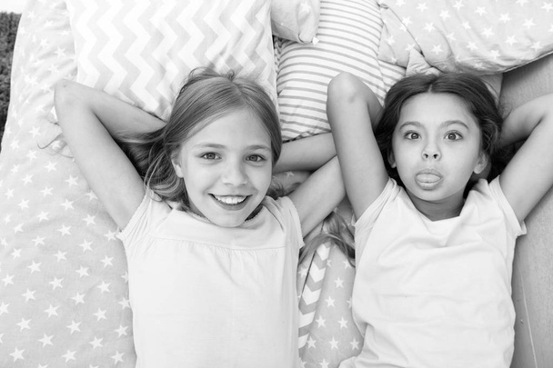 Best friends forever. Girls children lay on bed with cute pillows top view. Pajamas party concept. Girls in playful mood with grimace face. Friends children having fun together and feel comfortable - Foto, imagen
