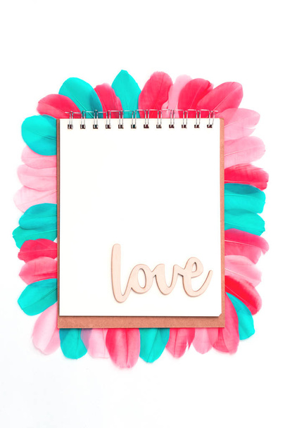 Creative layout with colorful feathers, love word and notebook. St Valentines, anniversary concept. Flat lay with copy space. - Photo, Image