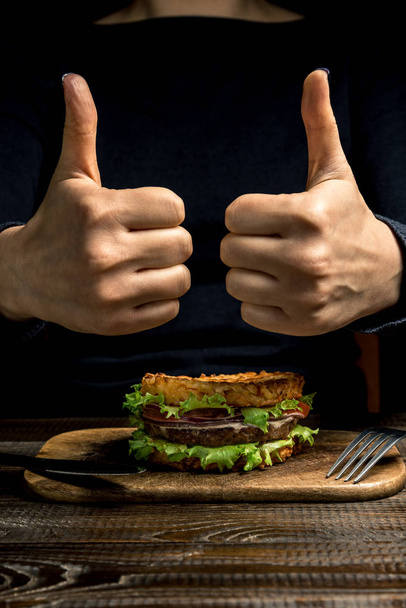 Mode de vie sain, bonne nutrition. Les mains féminines montrent "froides" sur un hamburger de riz sain avec des légumes, des herbes et des escalopes sur une planche en bois. Cadre vertical
 - Photo, image