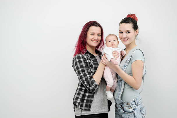 Two young women with a baby on a white background. Same-sex marriage and adoption, homosexual lesbian couple. - Фото, изображение