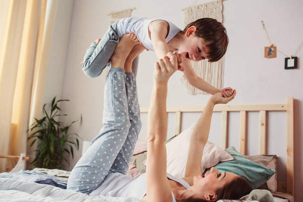 mother doing morning gymnastics with happy toddler son in bed. Happy family playing at home  - Valokuva, kuva