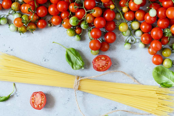 Cadre alimentaire. Concept d'ingrédients pour pâtes. Spaghettis non cuits et tomate cerise au basilic vert sur fond bleu. Vue supérieure avec espace de copie. Alimentation italienne
 - Photo, image