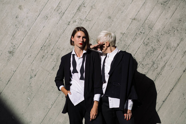  two women in classic suits posing against geometrical concrete wall outdoors  - Fotó, kép