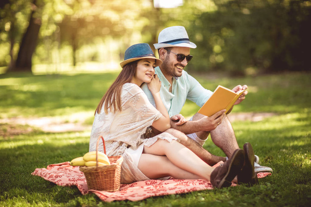 Beautiful couple enjoying picnic time outdoor reading book - Foto, Imagem
