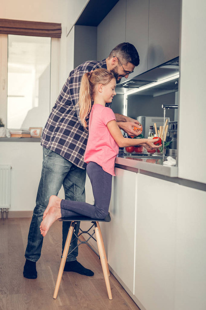 Long-haired pretty girl in a pink shirt and her father getting the breakfast ready - Foto, Imagen