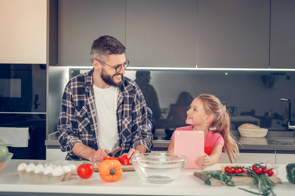 Tall bearded dark-haired man in a checkered shirt smiling to his daughter - Photo, image