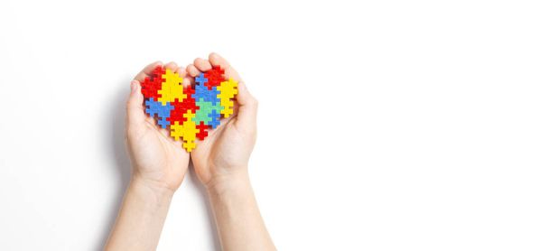 Mãos de criança segurando coração colorido no fundo branco. Conceito de Dia Mundial do Autismo - Foto, Imagem