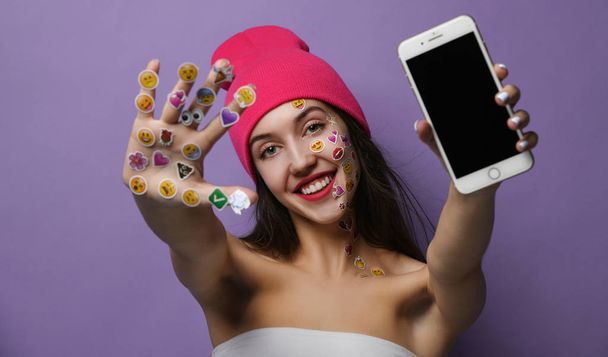 Woman with popular social mobile emoji smiles stickers for cellphone on her hands happy smiling laughing showing blank display screen - Foto, Imagem