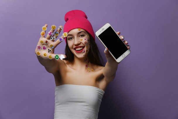 junge Frau mit beliebten Social-Mobile-Emoji lächelt Aufkleber für Handy auf ihren Händen glücklich lächelnd lachend zeigt leeren Bildschirm - Foto, Bild