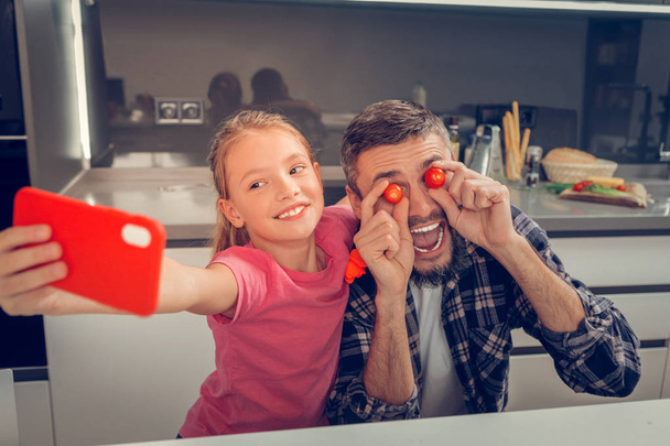 Tall bearded dark-haired father and his pretty daughter making selfie - 写真・画像